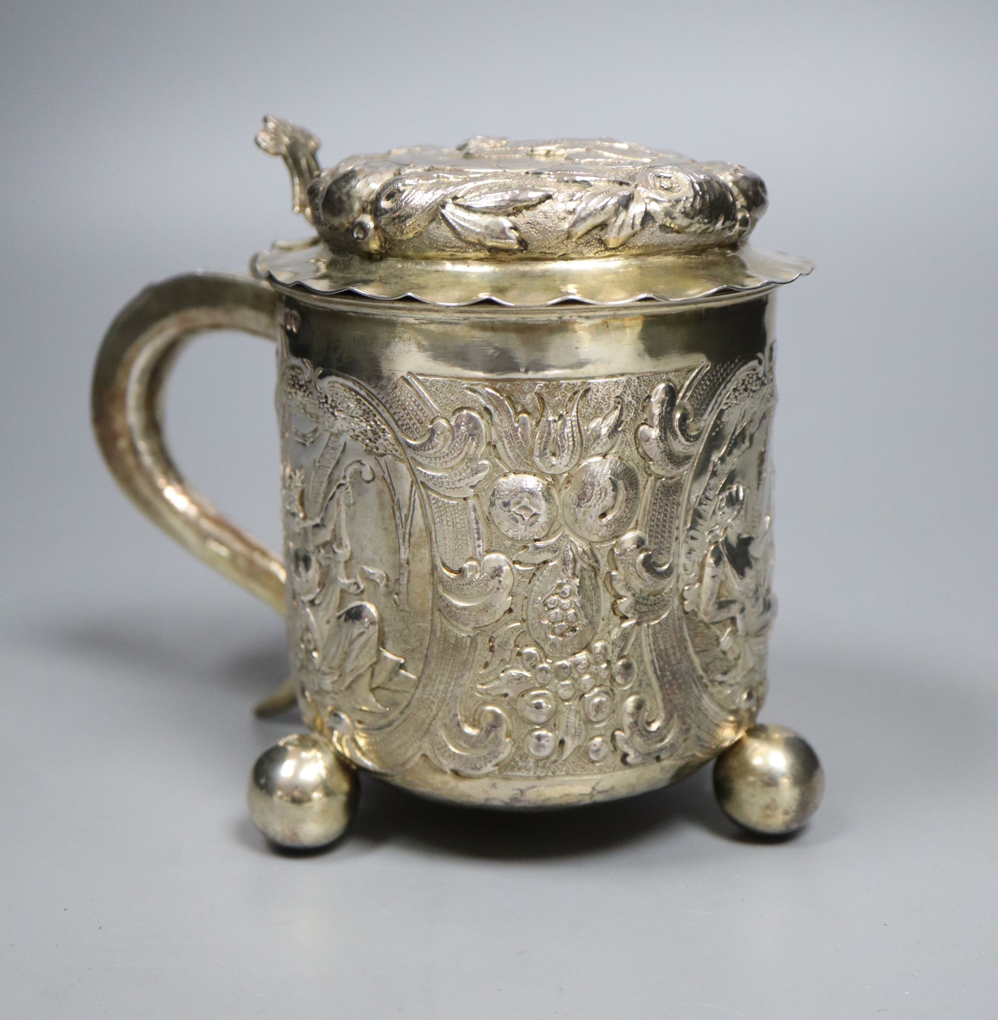 A late 19th century German? silver Scandinavian style embossed lidded tankard, on three ball feet,